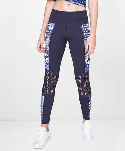 A woman stands against a plain background in Indigo Printed Leggings, featuring a stretchy polyblend fabric and vibrant blue print, paired with white sneakers.