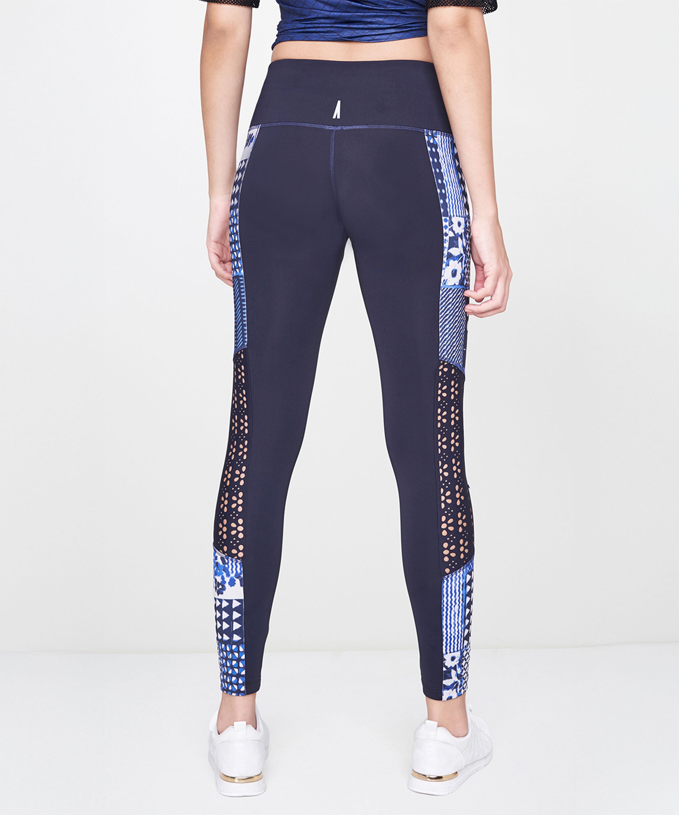 Someone wearing Indigo Printed Leggings, featuring a stretchy polyblend fabric with a vibrant blue print, paired with white sneakers and shown from the back against a plain background.