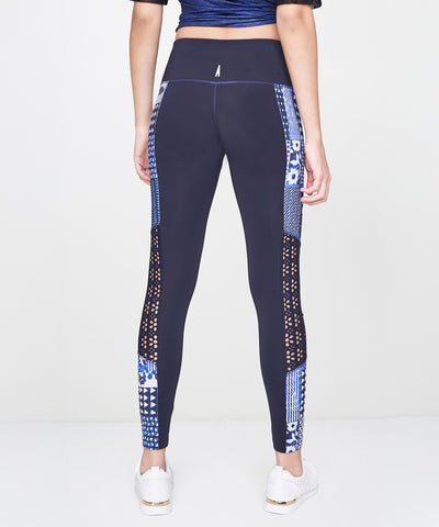 Someone wearing Indigo Printed Leggings, featuring a stretchy polyblend fabric with a vibrant blue print, paired with white sneakers and shown from the back against a plain background.
