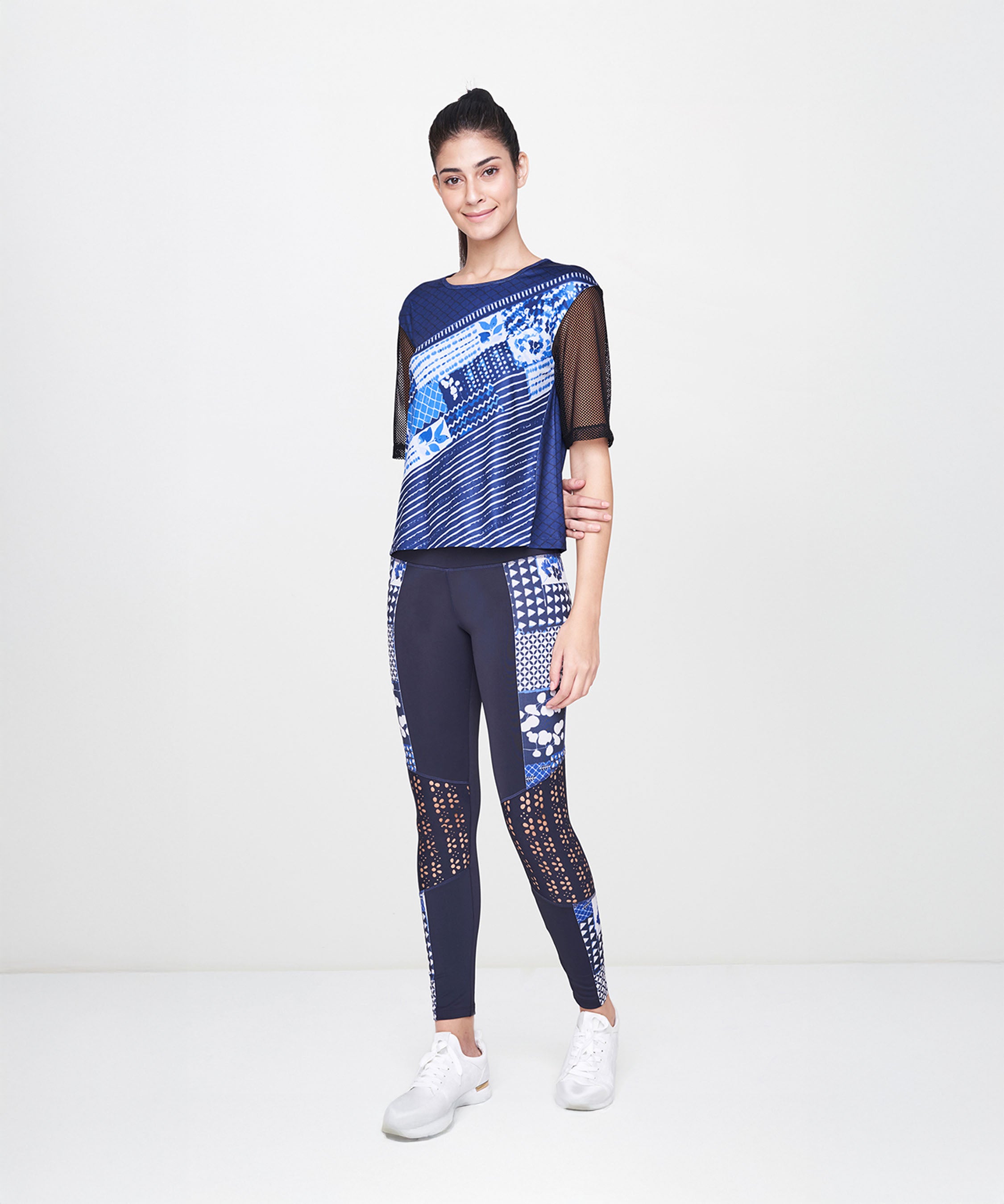 Woman smiles while wearing the Indigo Printed Top With Leggings and white sneakers, standing against a plain white background.