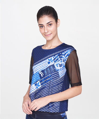 Woman wearing an Indigo Printed Top with net sleeves, smiling and standing against a plain white background.