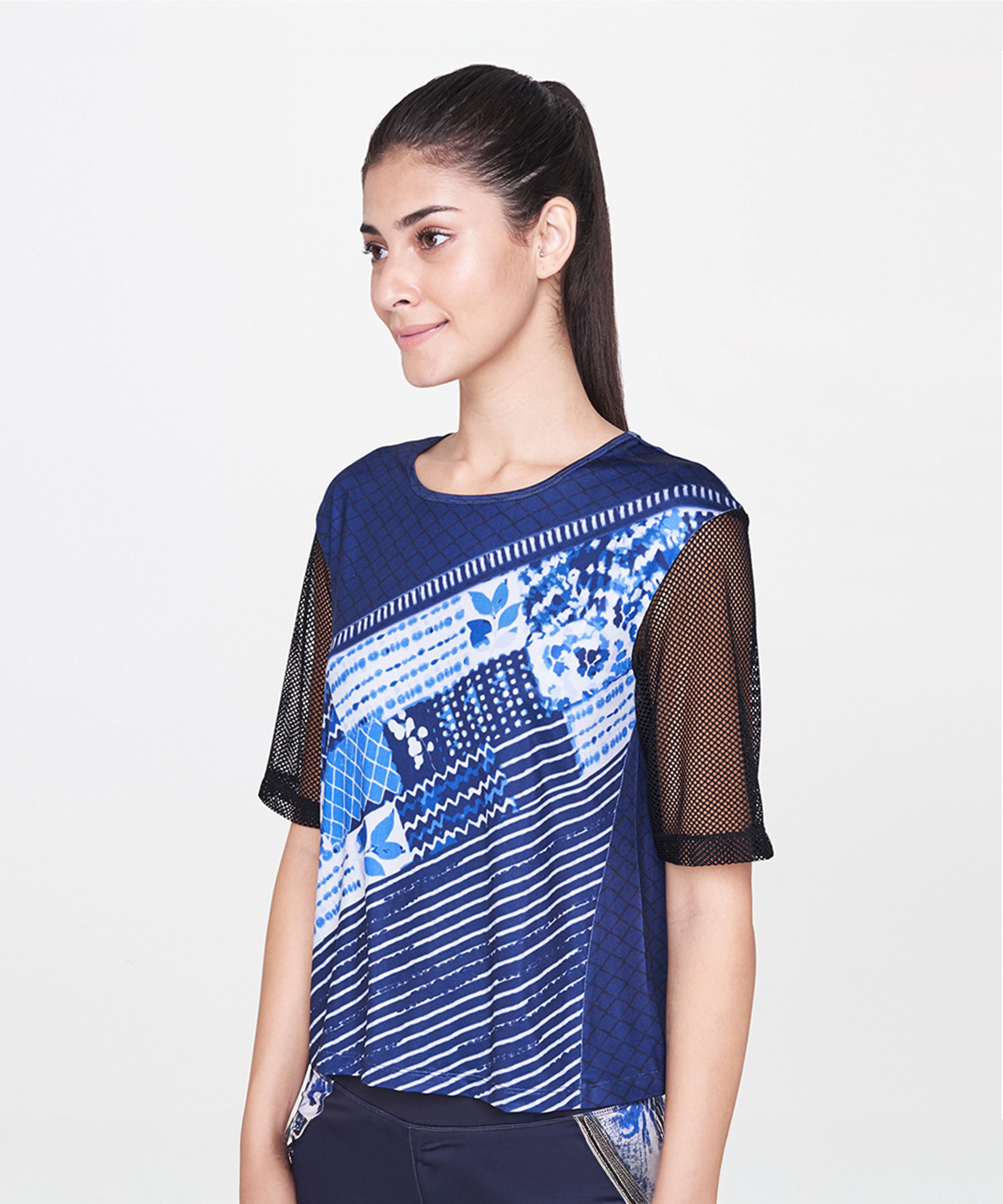Woman wearing an Indigo Printed Top with black net sleeves, standing and smiling against a white background.