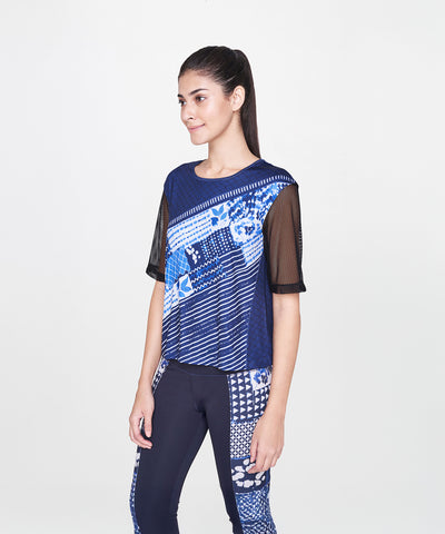 Woman wearing the Indigo Printed Top With Leggings, featuring a blue patterned design and net sleeves, standing and smiling against a plain white background.
