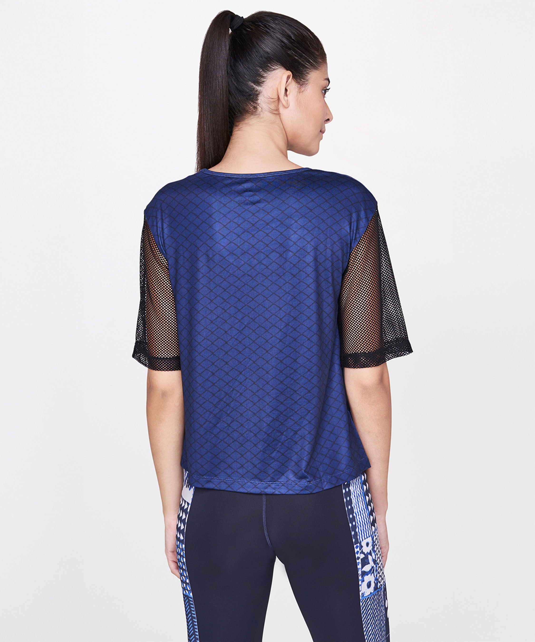 Woman with a ponytail, facing away, wearing the Indigo Printed Top with net sleeves and patterned leggings.