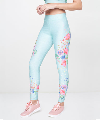 A woman stands against a plain white background wearing Aqua Printed Leggings and pink sneakers.