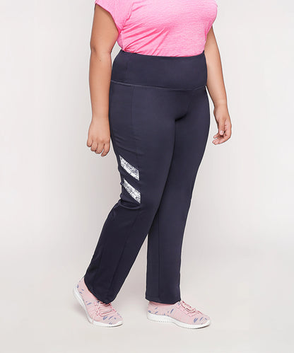 A woman stands against a light background wearing a pink shirt, pink sneakers, and Tuna London Iris Navy Polyblend Track Pant for women.