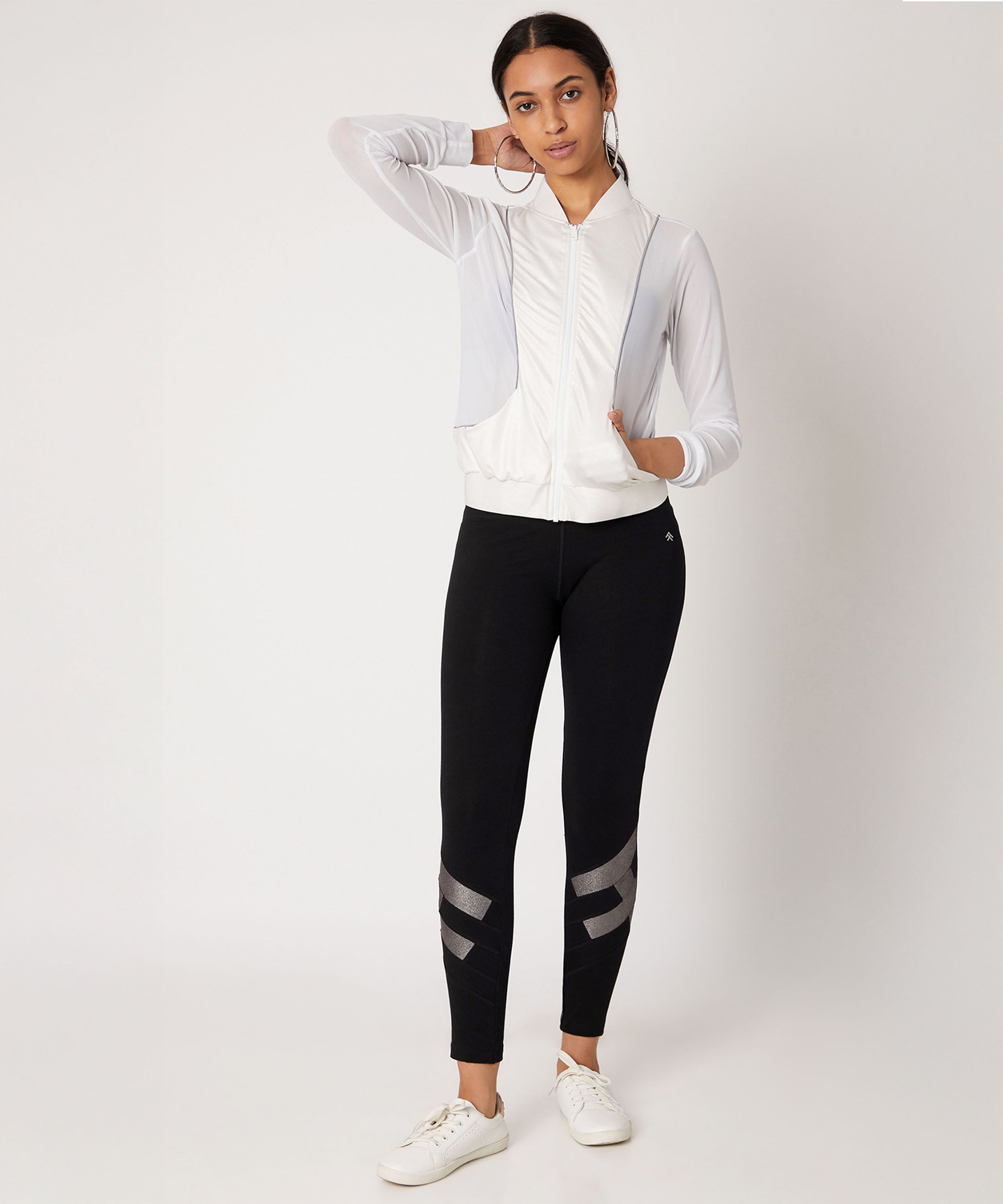 A woman in a white zip-up jacket and Black High Waisted Leggings With a Metallic Touch stands against a plain background.