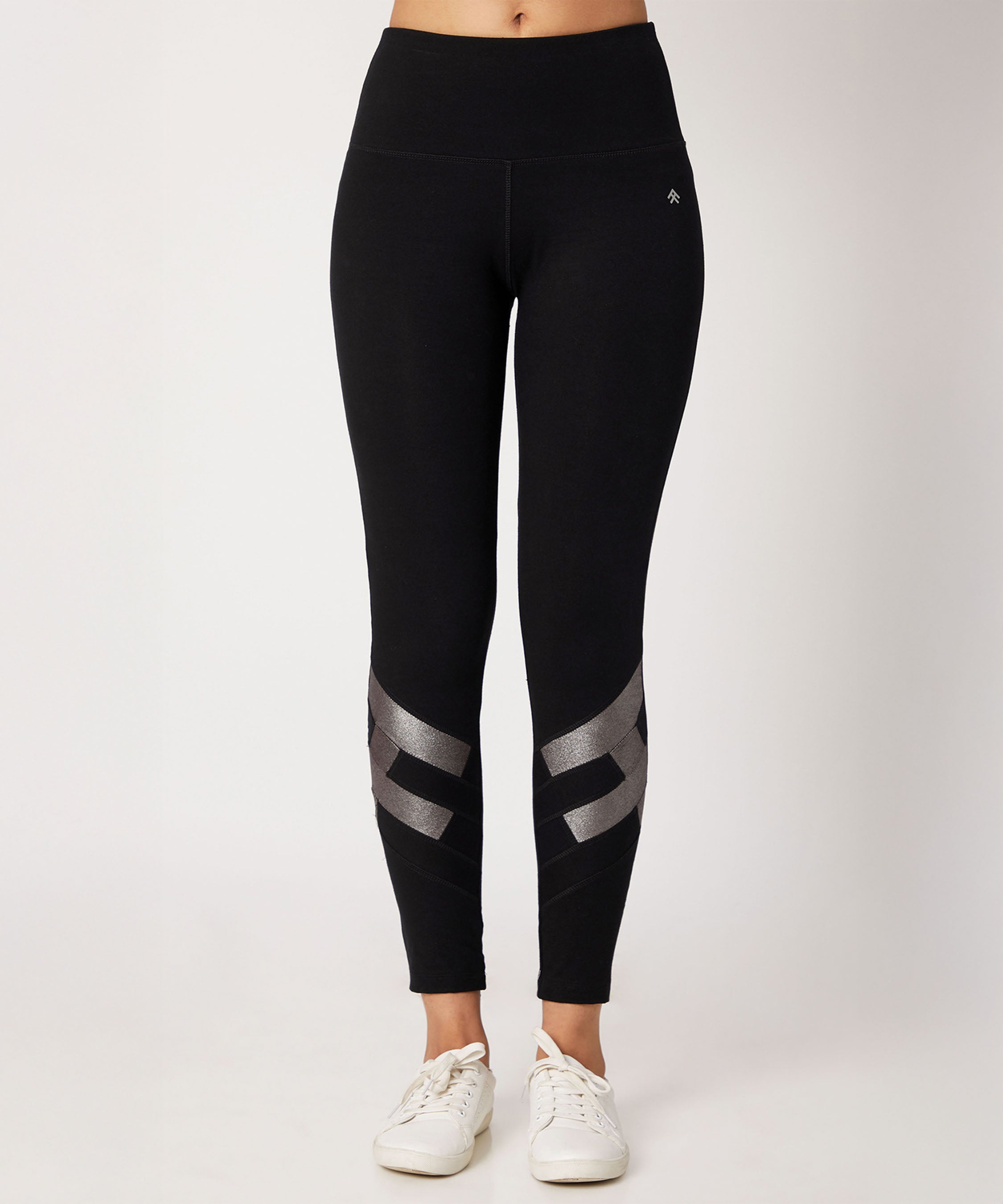 Model wears the Black High Waisted Leggings With a Metallic Touch, featuring metallic details near the ankles and four-way stretch fabric for comfort and style, paired with white sneakers against a plain background.