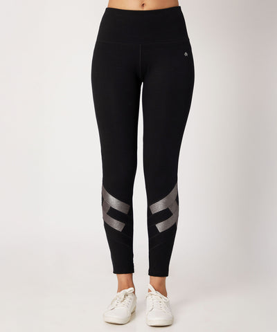 Model wears the Black High Waisted Leggings With a Metallic Touch, featuring metallic details near the ankles and four-way stretch fabric for comfort and style, paired with white sneakers against a plain background.