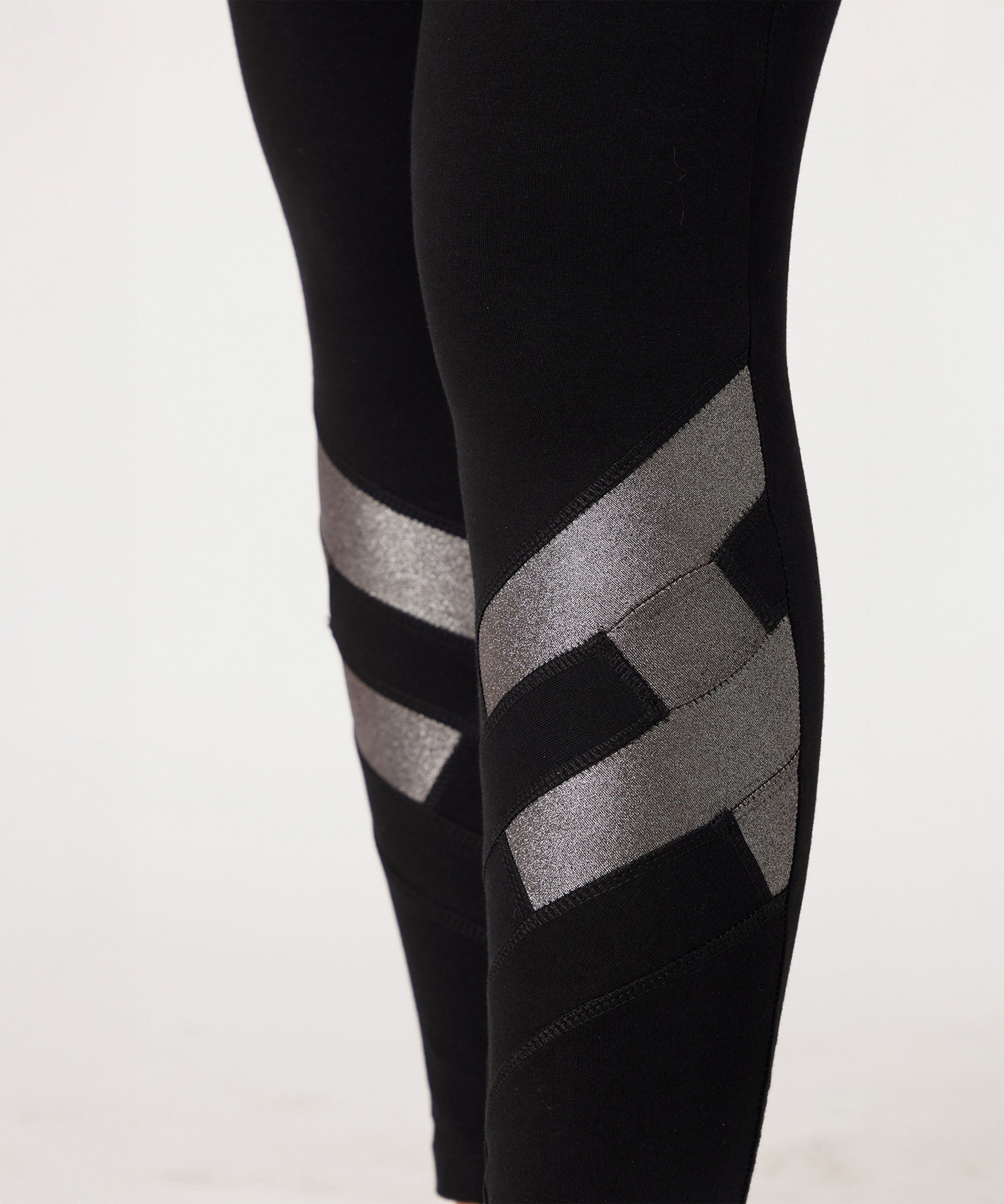 Black High Waisted Leggings With a Metallic Touch feature shiny silver geometric patterns and metallic detailing on the lower legs, crafted from four-way stretch fabric and displayed against a plain background.
