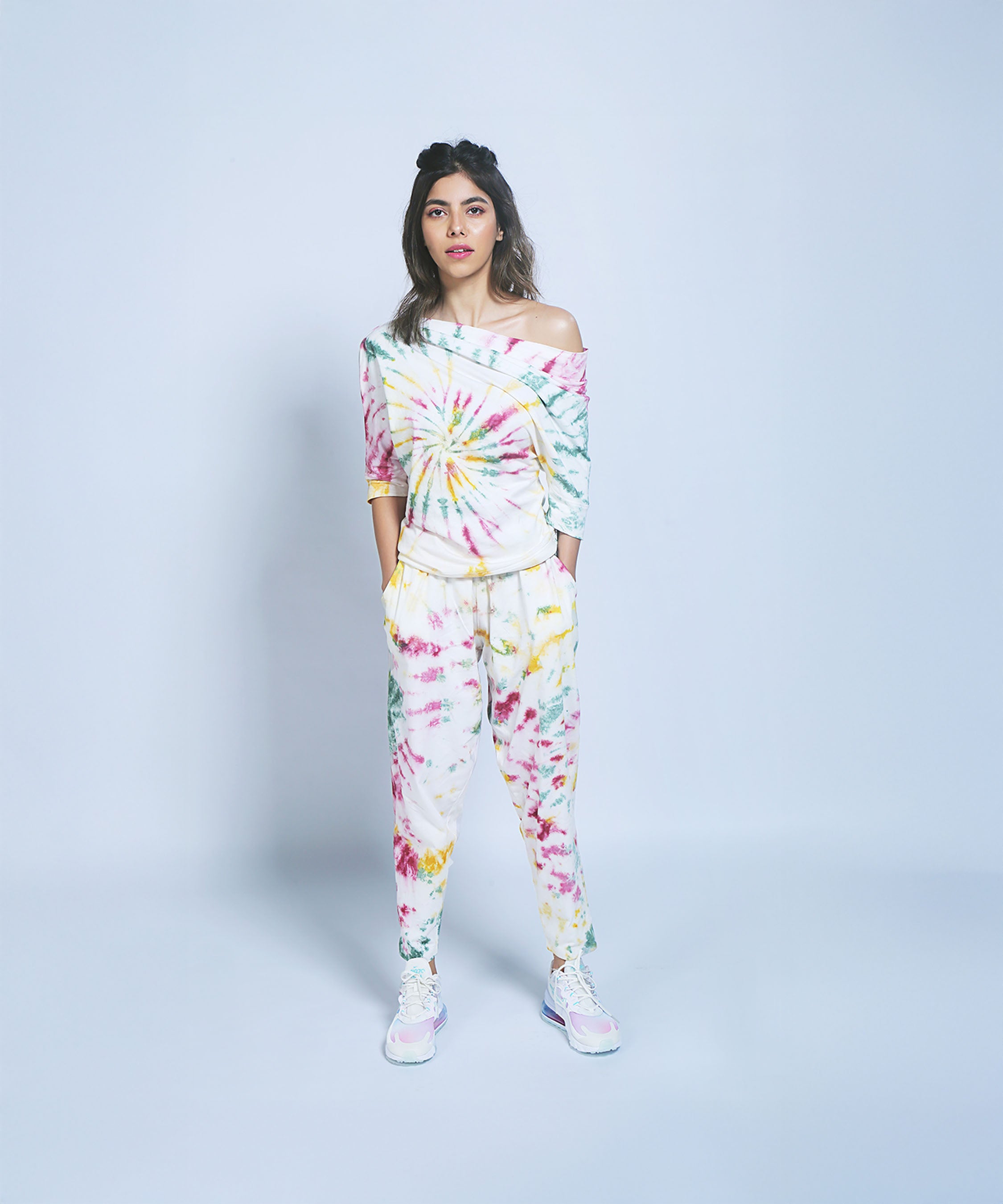 Woman wearing the One Side Off-Shoulder top and Yoga Pants set, featuring a colorful tie-dye pattern and organic cotton, hands in pockets against a plain light background.
