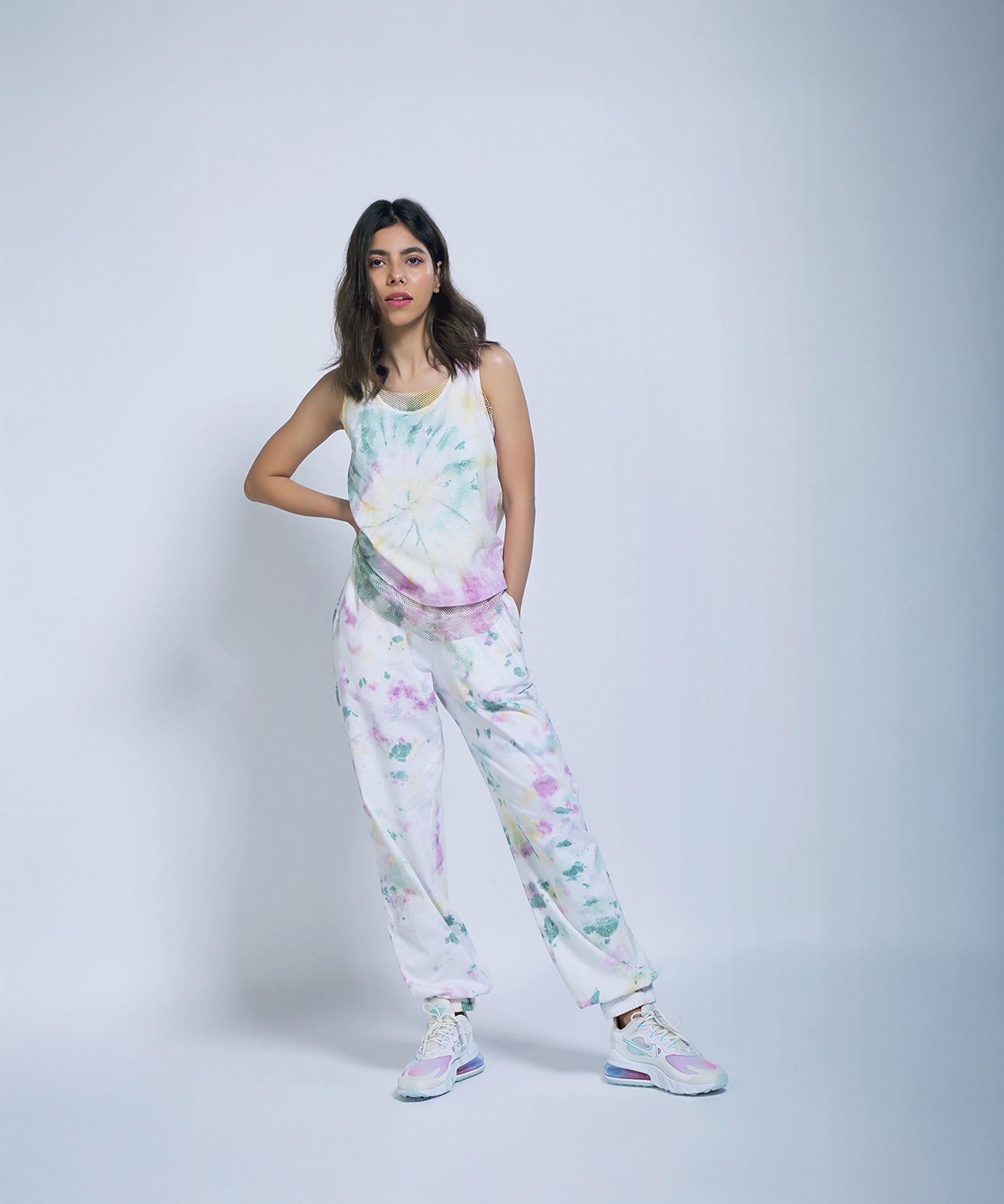 Woman wears the Comfort Fit Joggers + Netted Tank Top, crafted from organic cotton, standing with one hand in her pocket against a light background.