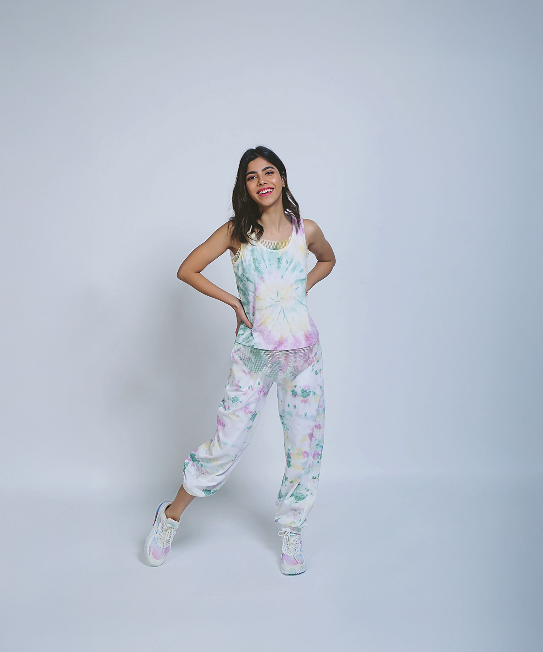 Woman wearing Comfort Fit Joggers and a Netted Tank Top, smiling and posing against a plain light background.