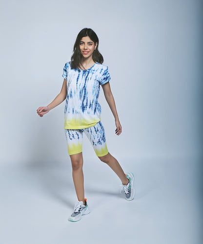 Woman wearing the Comfort Fit Tee/Sweatshirt and Biker Shorts set, both in tie-dye cotton, paired with sneakers, walking against a light gray background.