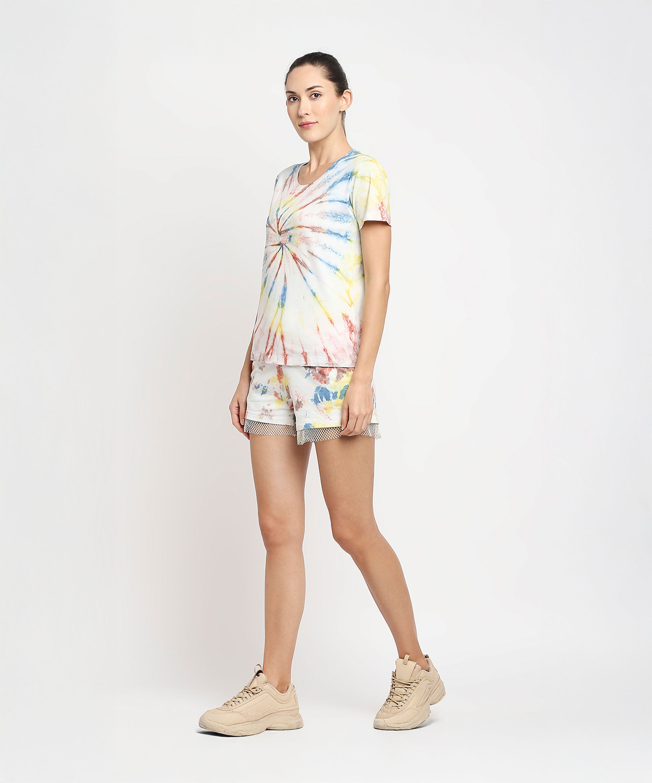 A woman stands against a white background wearing Netted shorts and a comfort tee made with eco-friendly dyes, paired with beige sneakers.