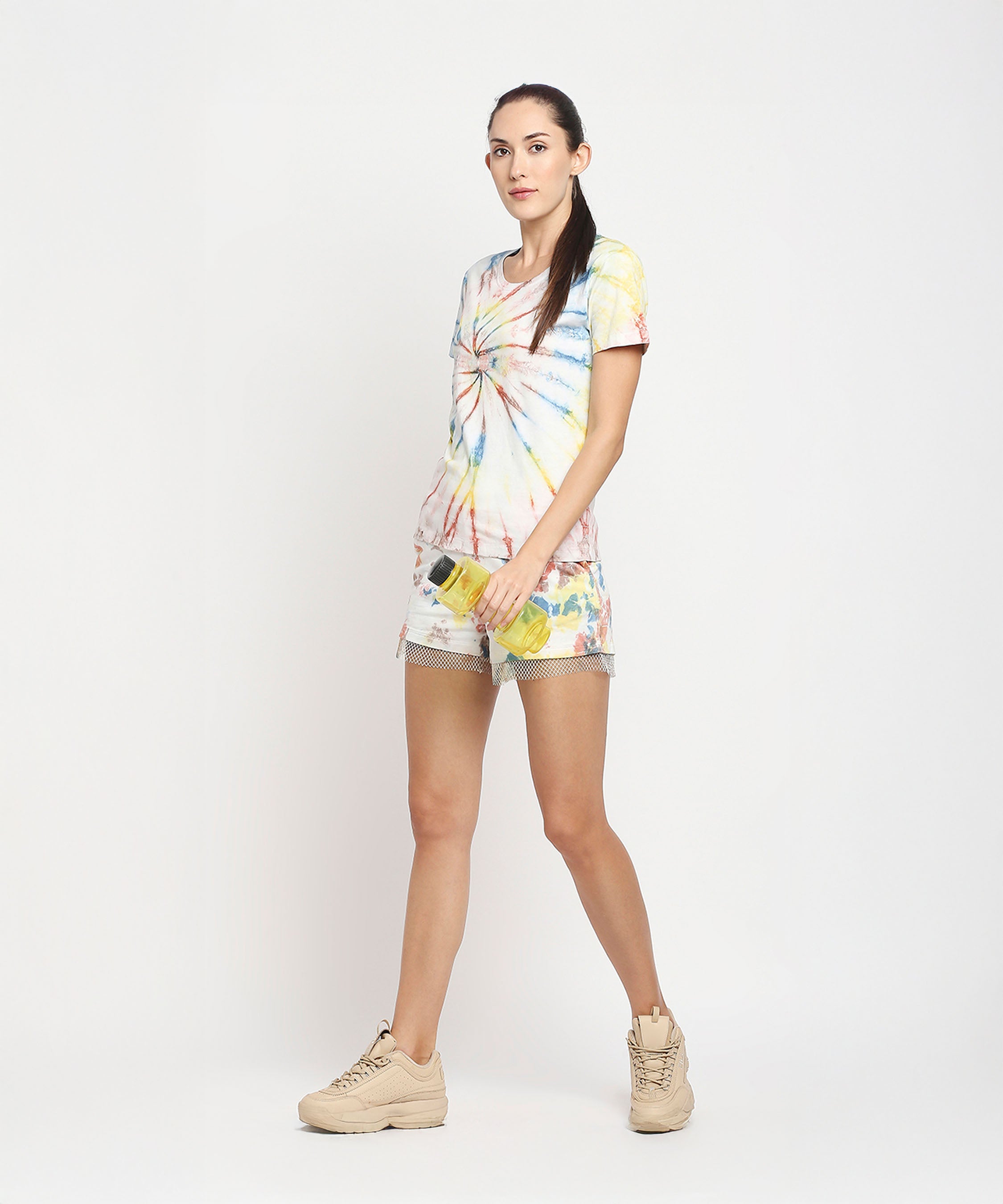 Woman wears Netted shorts and a comfort tee made with eco-friendly dyes, holding a yellow water bottle against a plain white background.