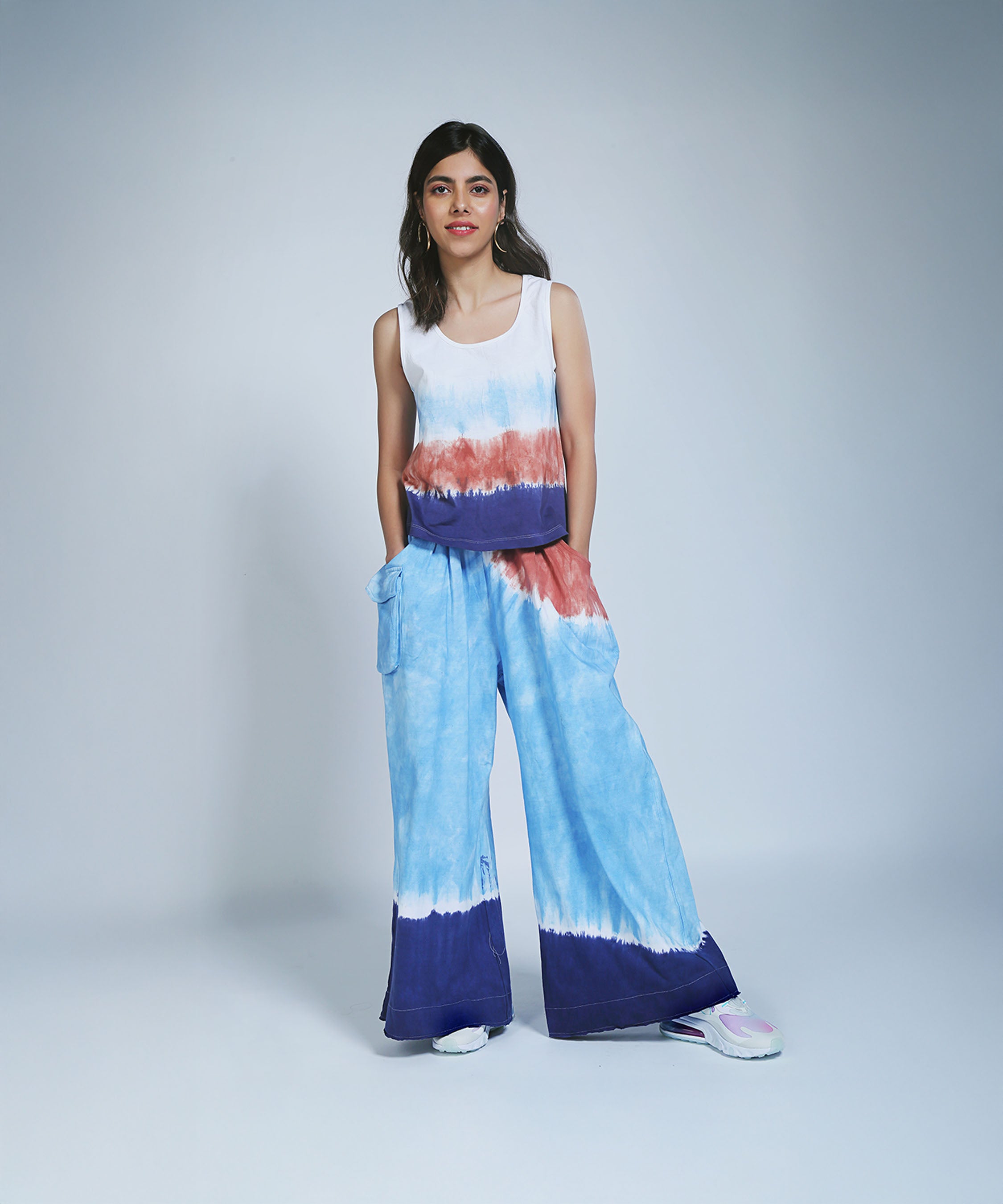 A woman wears the Cargo Pocket Parallels and Comfort Fit Tank Top, both hand-dyed with blue, white, and red patterns, standing against a plain background.