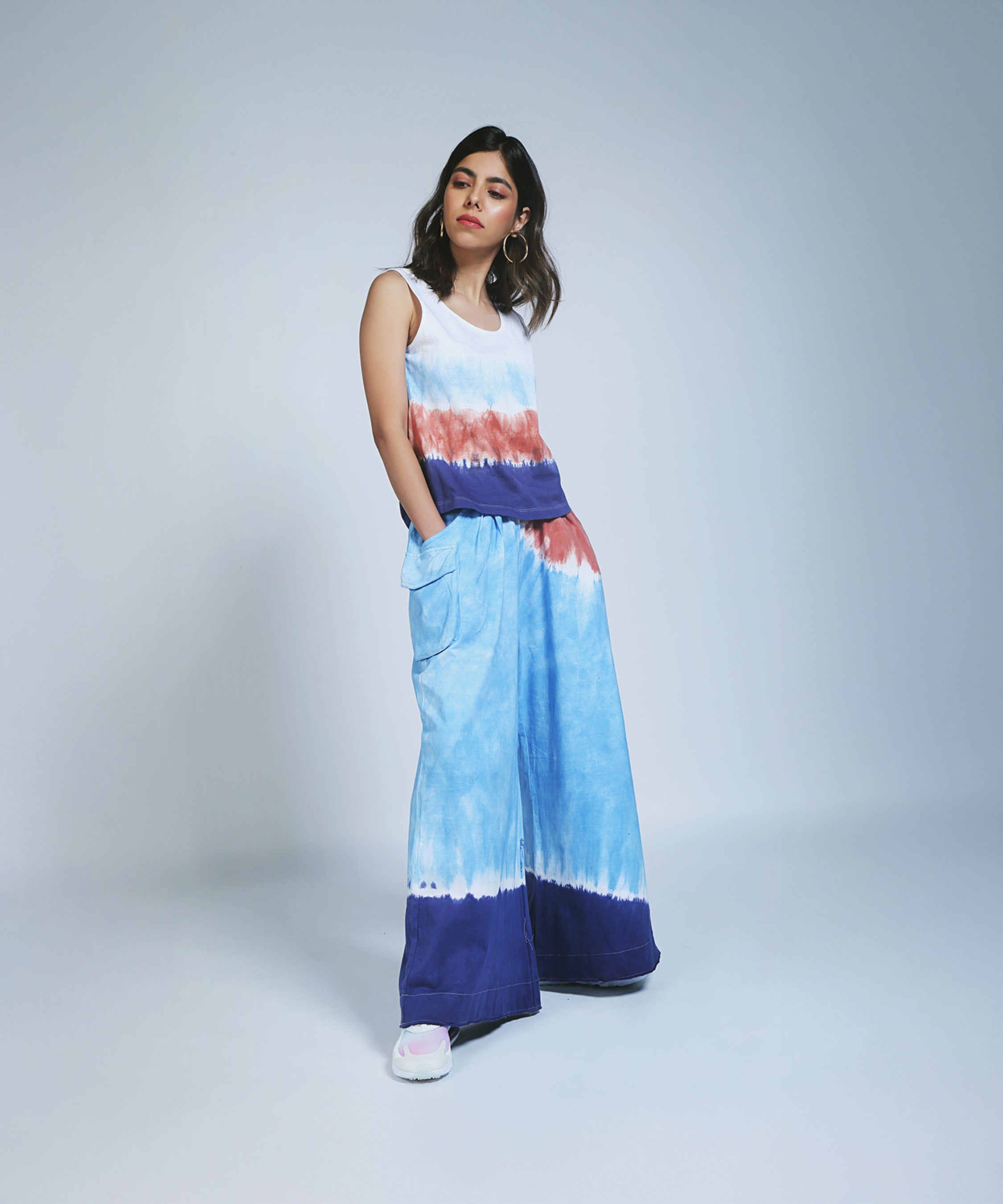A woman models the Cargo Pocket Parallels and Comfort Fit Tank Top in hand-dyed blue and white cotton, standing in a studio.