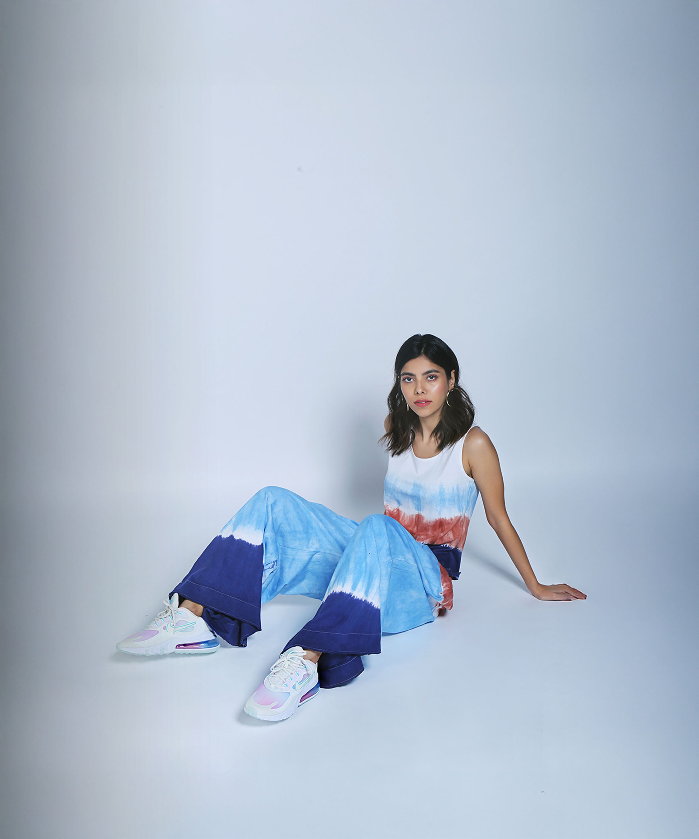 A woman wears the Cargo Pocket Parallels and Comfort Fit Tank Top, sitting on a white floor against a plain background, looking at the camera.