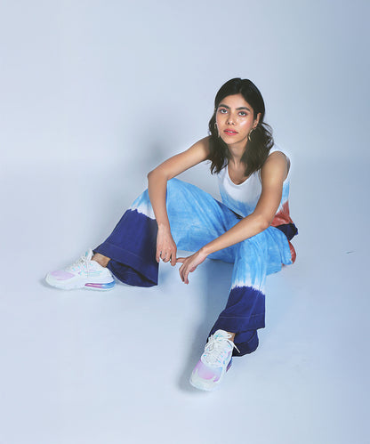 Woman in a Comfort Fit Tank Top and Cargo Pocket Parallels in blue and white tie-dye, sitting on the floor and looking at the camera against a plain background.