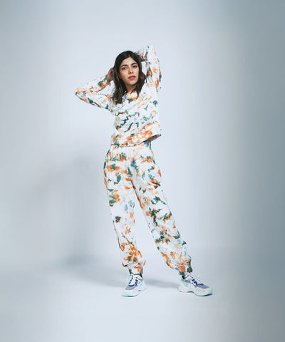 A woman in an Earthy Tones Sweatshirt / Tee and Comfort Joggers with white sneakers stands hands behind her head against a light backdrop.
