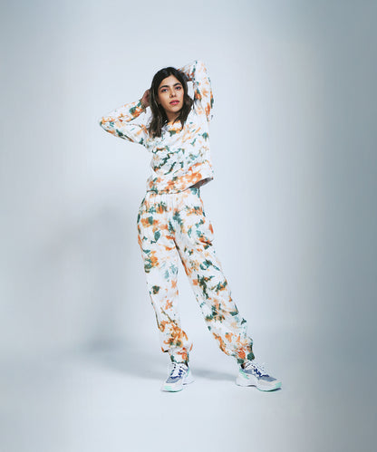 A woman in an Earthy Tones Sweatshirt / Tee and Comfort Joggers with white sneakers stands hands behind her head against a light backdrop.
