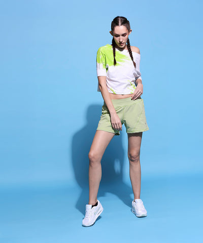 Woman wears the One side Off Shoulder Crop Top With Shorts- AW21 in lime green, posing against a solid light blue background.