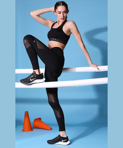 A woman poses confidently in Netted High Rise Compression Leggings–AW21 on white bars with orange cones, set against a vibrant blue background.