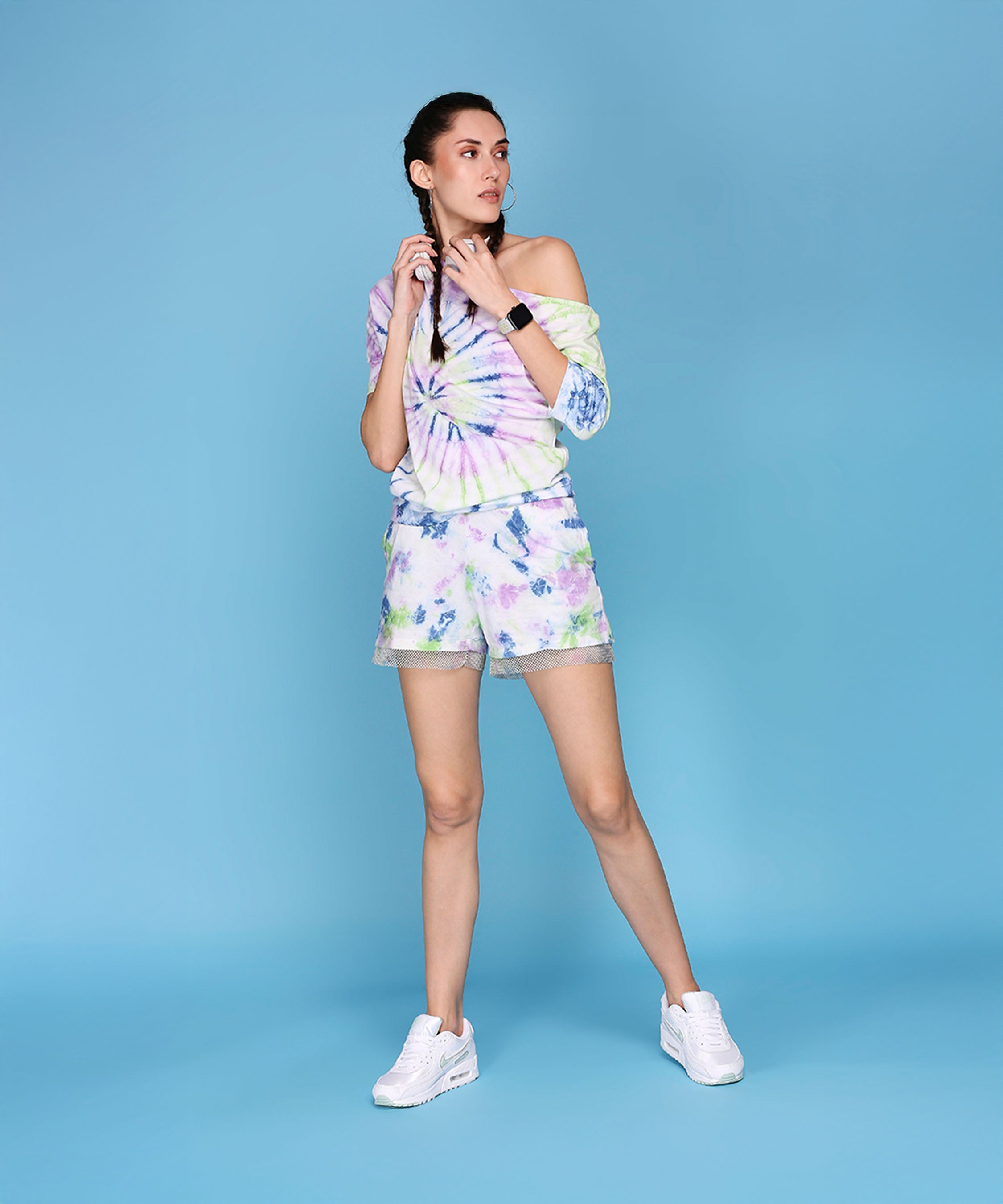 A woman poses against a blue background wearing the One Side Off-Shoulder With Netted Shorts - AW21 set, paired with white sneakers for a bold autumn-winter look.
