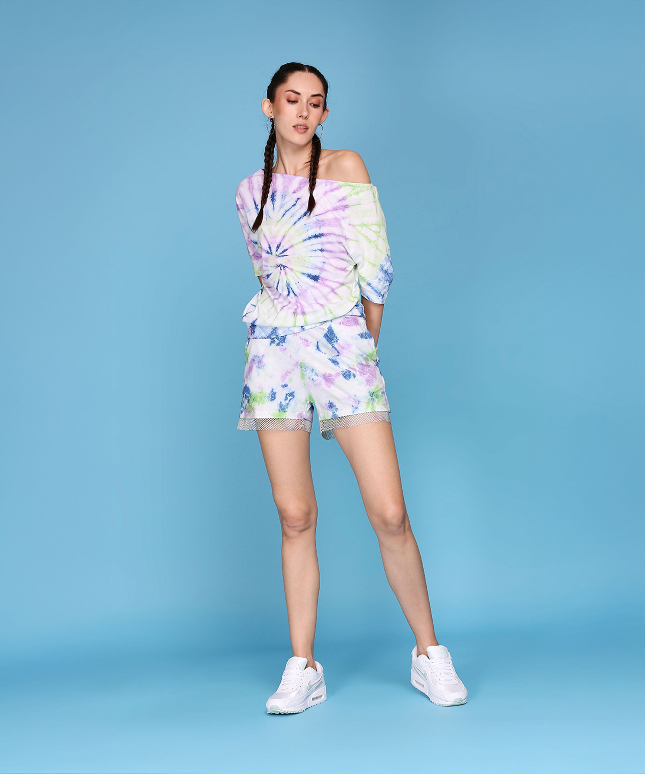 Woman wearing the One Side Off-Shoulder With Netted Shorts - AW21 set, paired with white sneakers, stands against a blue background.