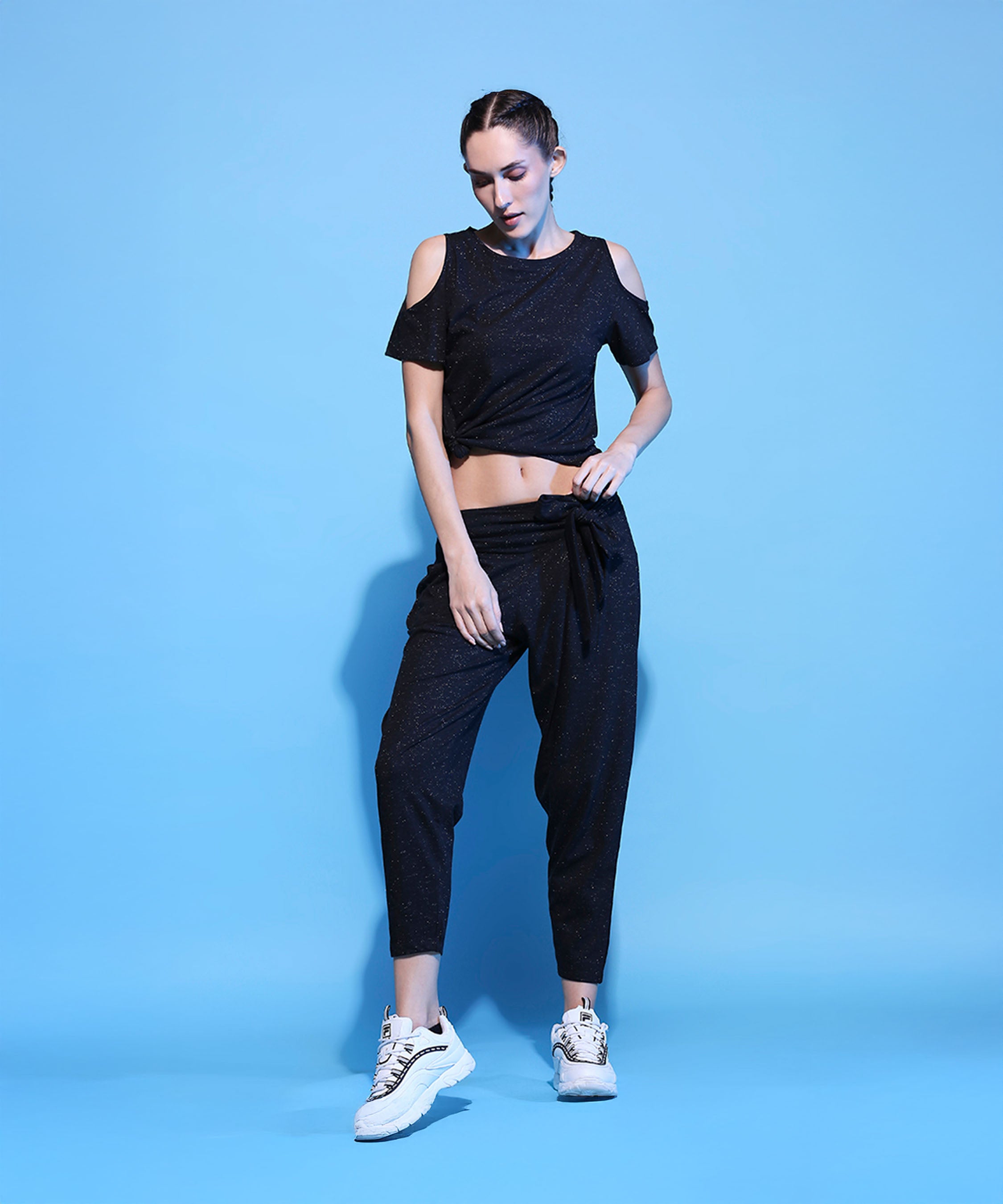 A woman in a Shimmer Cold Shoulder Tee (Customised) paired with Side Tie Up Shimmer Yoga Pants- AW21.