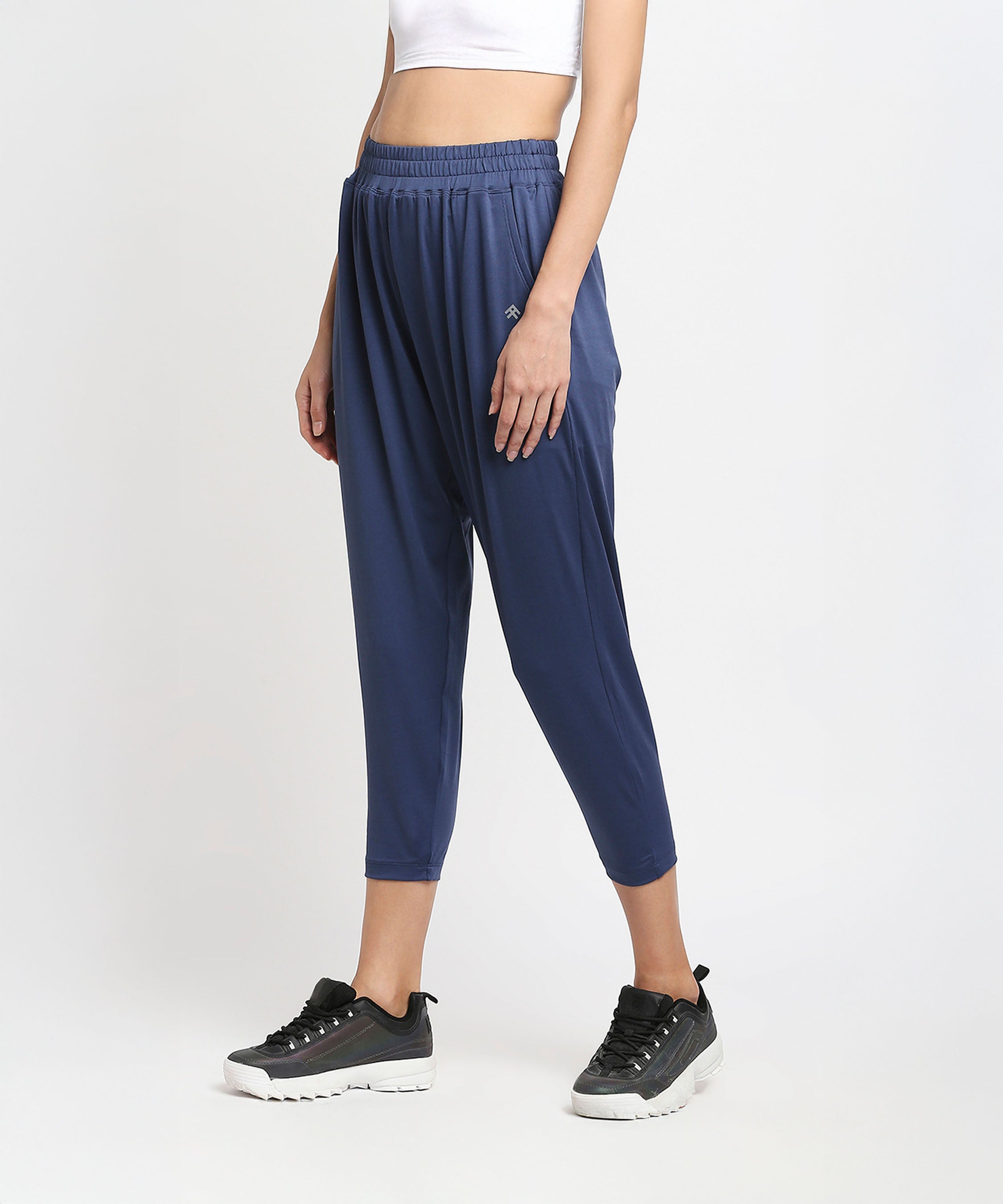Woman in relaxed fit Blue Yoga Pants - AW21, a white crop top, and black sneakers stands against a plain background.