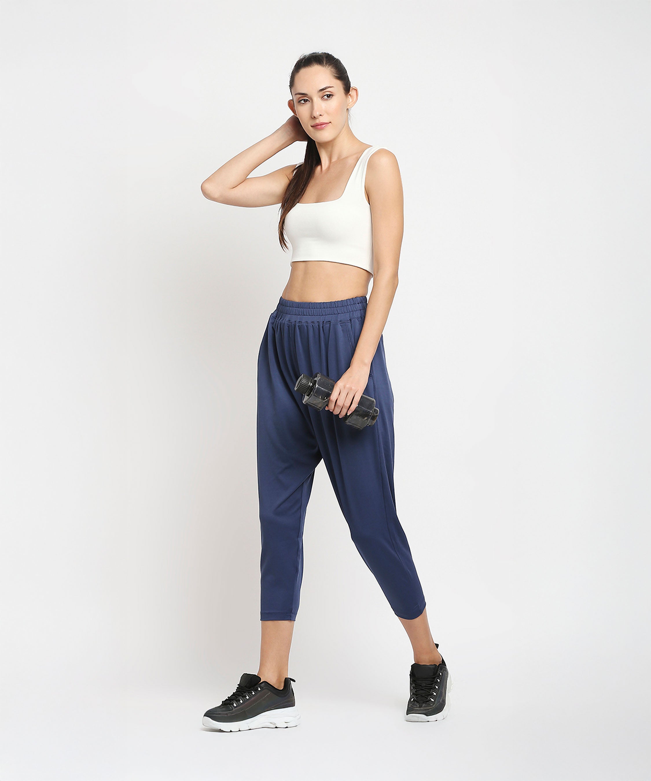Woman in workout clothes holding a dumbbell, standing against a plain white background, wearing Blue Yoga Pants - AW21 for ultimate comfort during any workout.