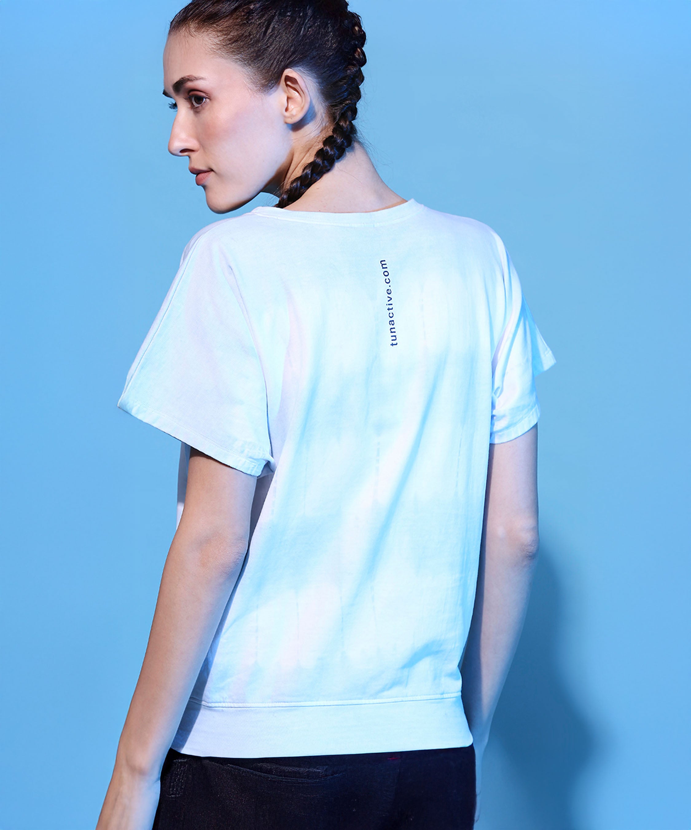 Woman with braided hair faces away, modeling the Barcode Printed Comfort Tie Dye Tee + Joggers - AW21 set against a blue background.