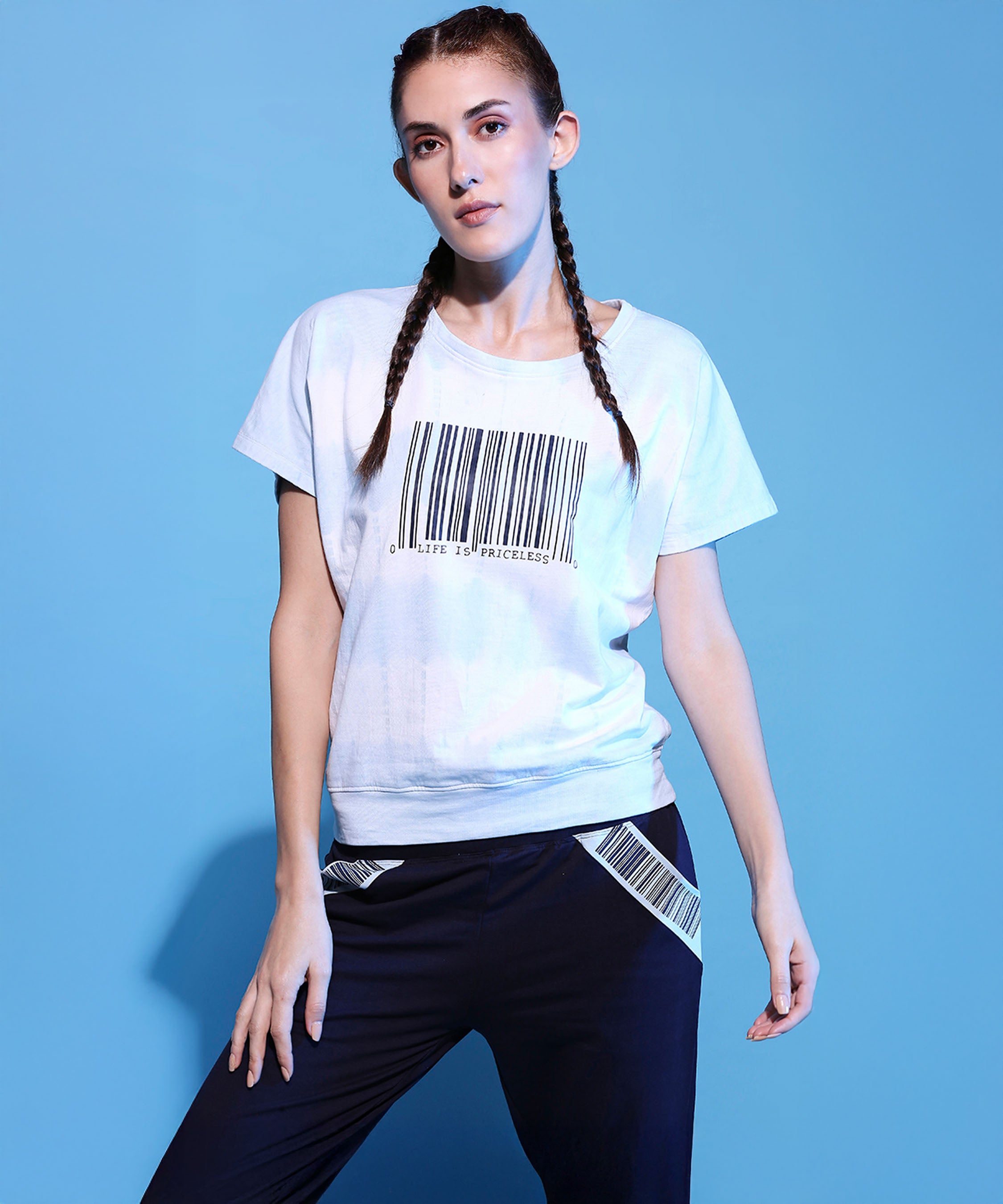 A woman with braided hair stands on a blue background wearing the Barcode Printed Comfort Tie Dye Tee + Joggers – AW21 set.