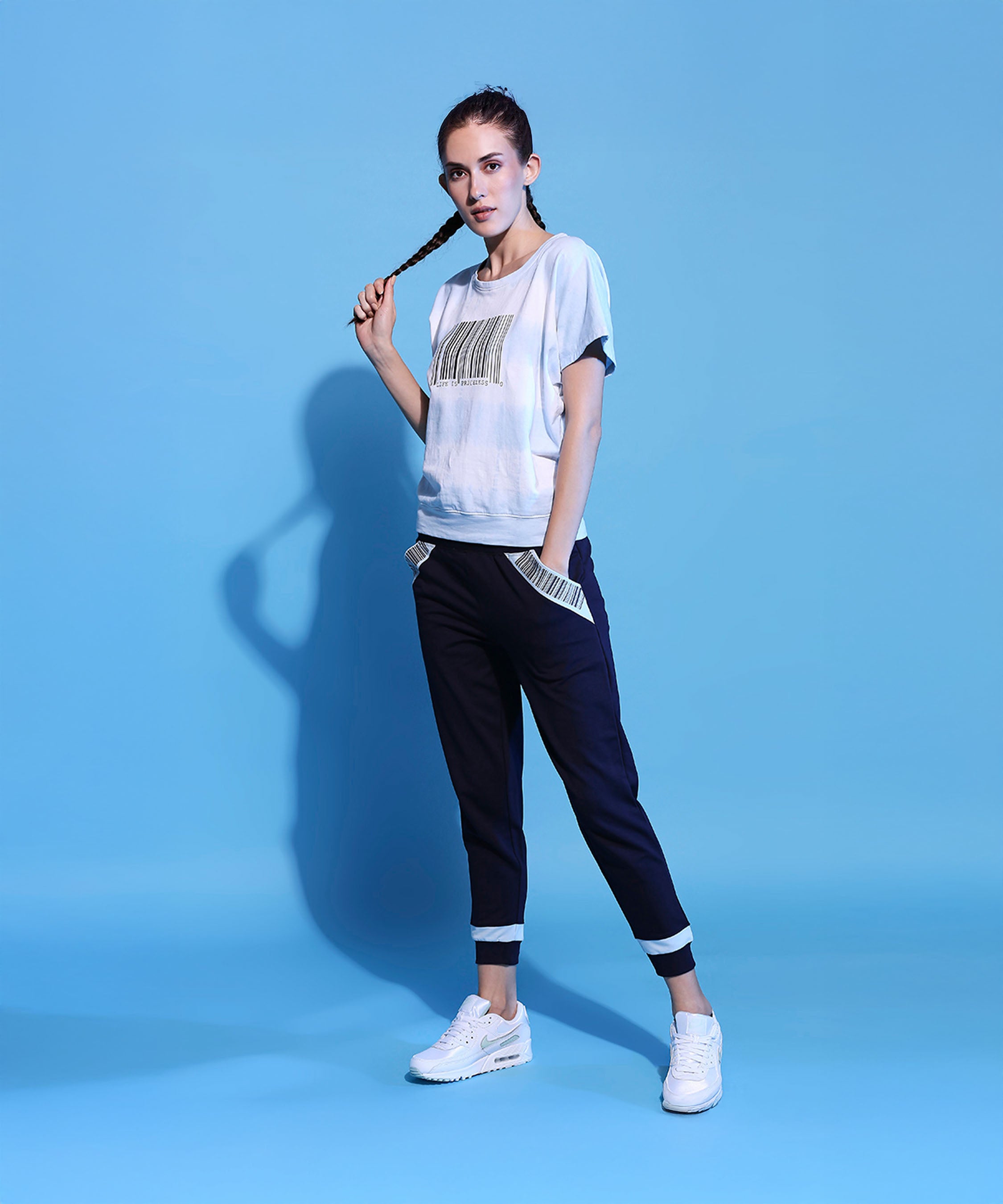 Woman in a Barcode Printed Comfort Tie Dye Tee + Joggers - AW21 stands against a blue background, holding her braided hair.
