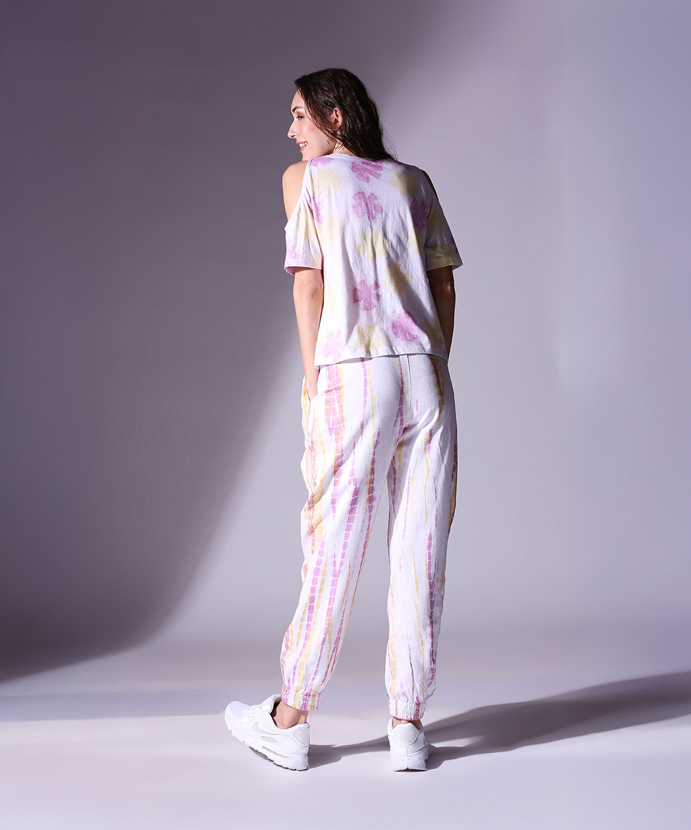 Woman wearing the Cold Shoulder Tee + Joggers - AW21 and white sneakers stands smiling, facing away from the camera.