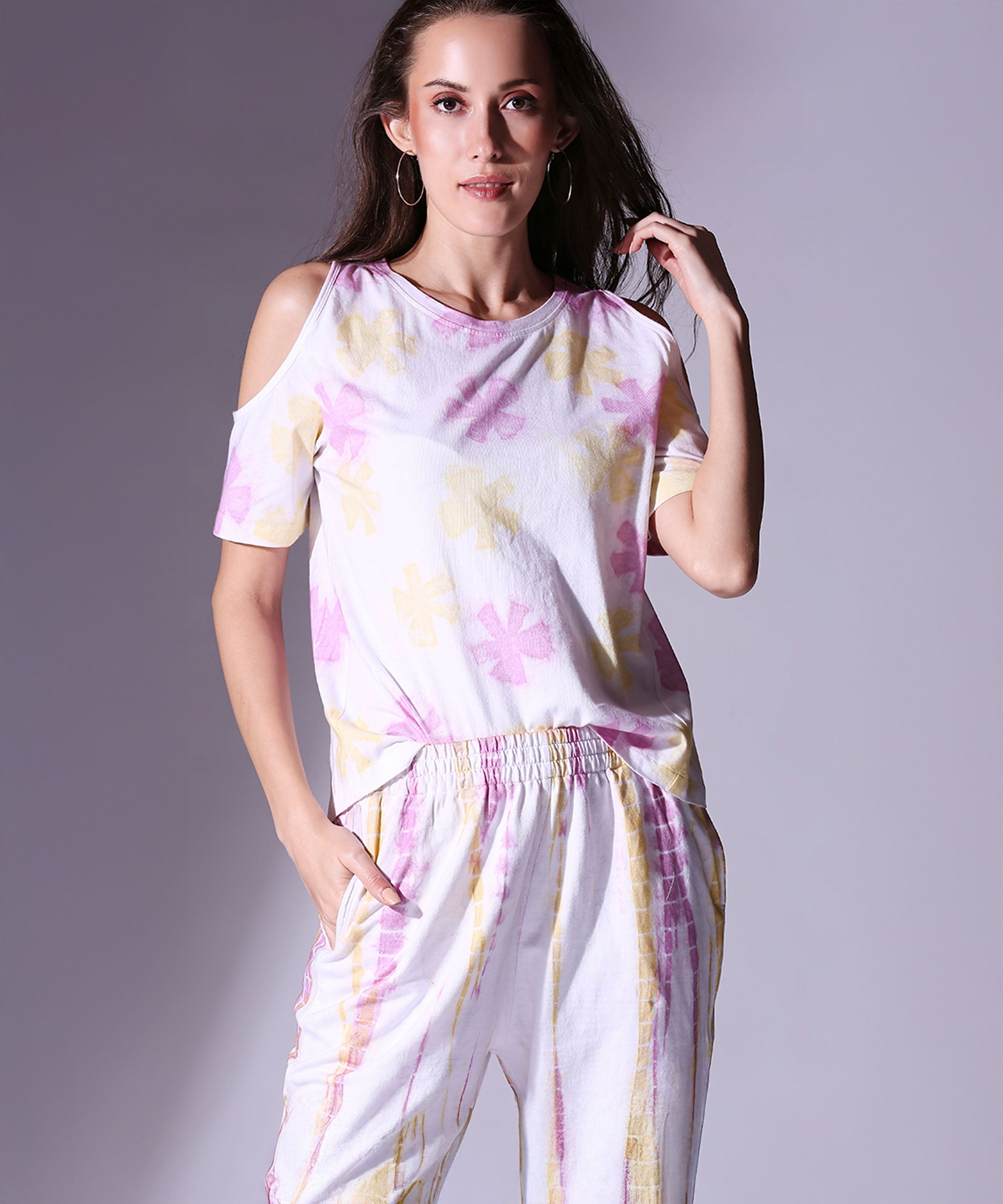 Woman wearing the Cold Shoulder Tee + Joggers - AW21, featuring a white floral cold shoulder top and matching joggers, standing with one hand in her pocket.