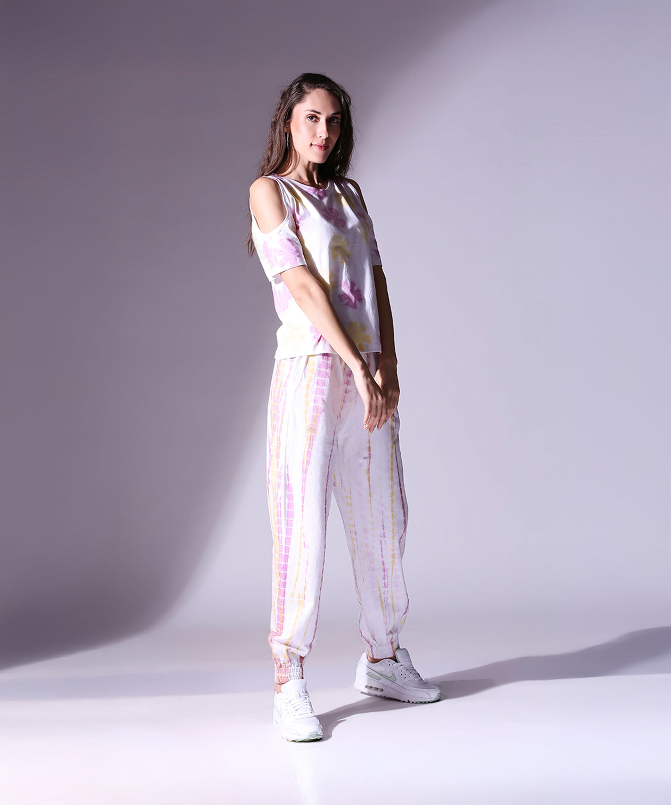 Woman poses confidently in the Cold Shoulder Tee + Joggers - AW21, styled with white sneakers against a plain backdrop.