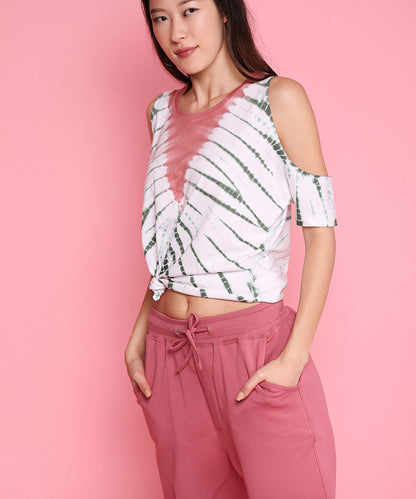 A woman poses in the Cold Shoulder Comfort Fit Top + Joggers - AW21, a stylish pink athleisure set, set against a solid pink background.