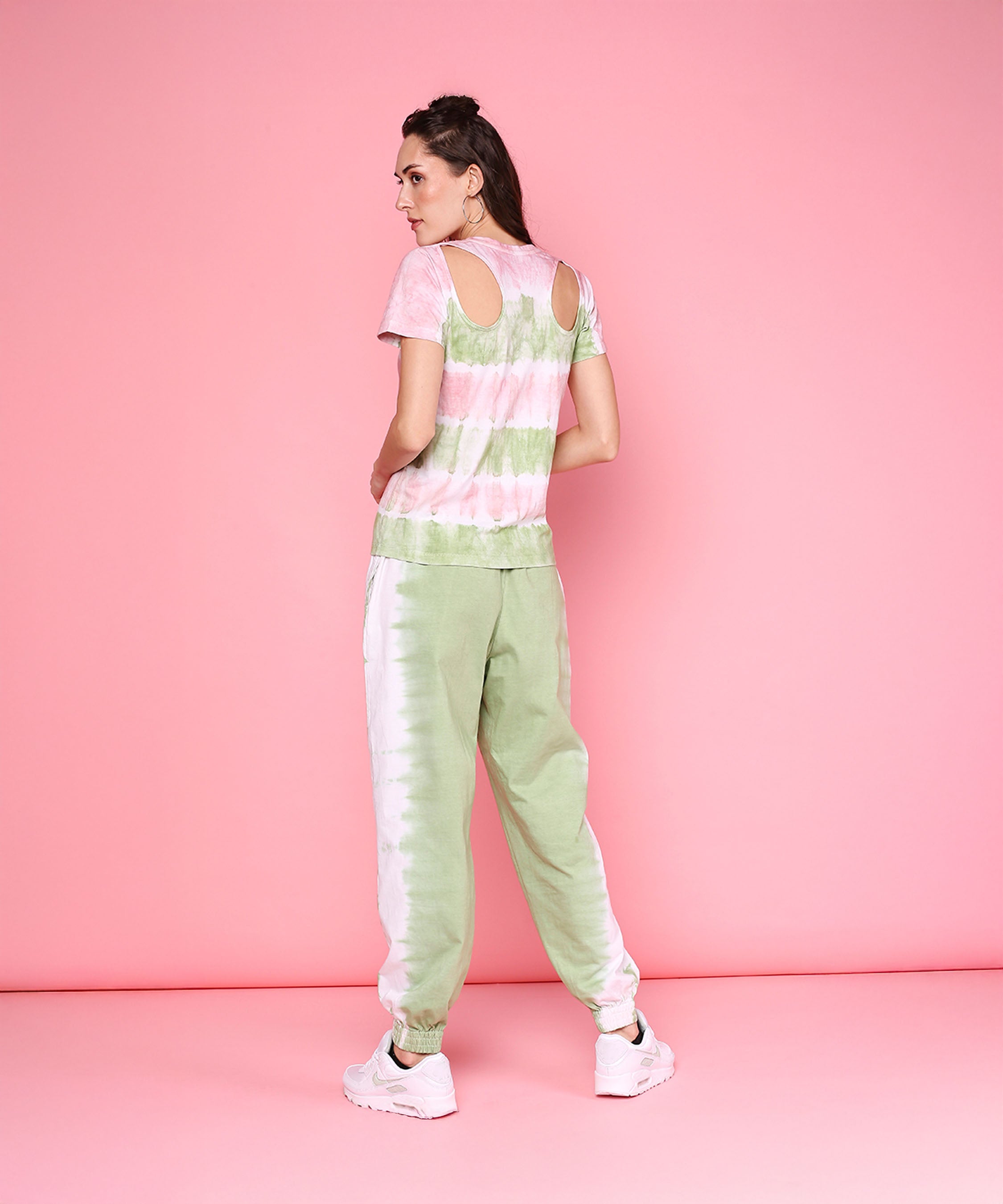 Model wears the Tee With Racer Back Cut + Joggers - AW21, featuring hand-dyed fabric and back cutouts, paired with mint green joggers. She stands on a pastel pink background with her back facing the camera.