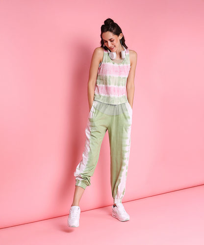 Woman in the Comfort Fit Joggers + Netted Tank Top - AW21, featuring pink and mint green pastel hues, paired with white sneakers, stands smiling against a pink background.