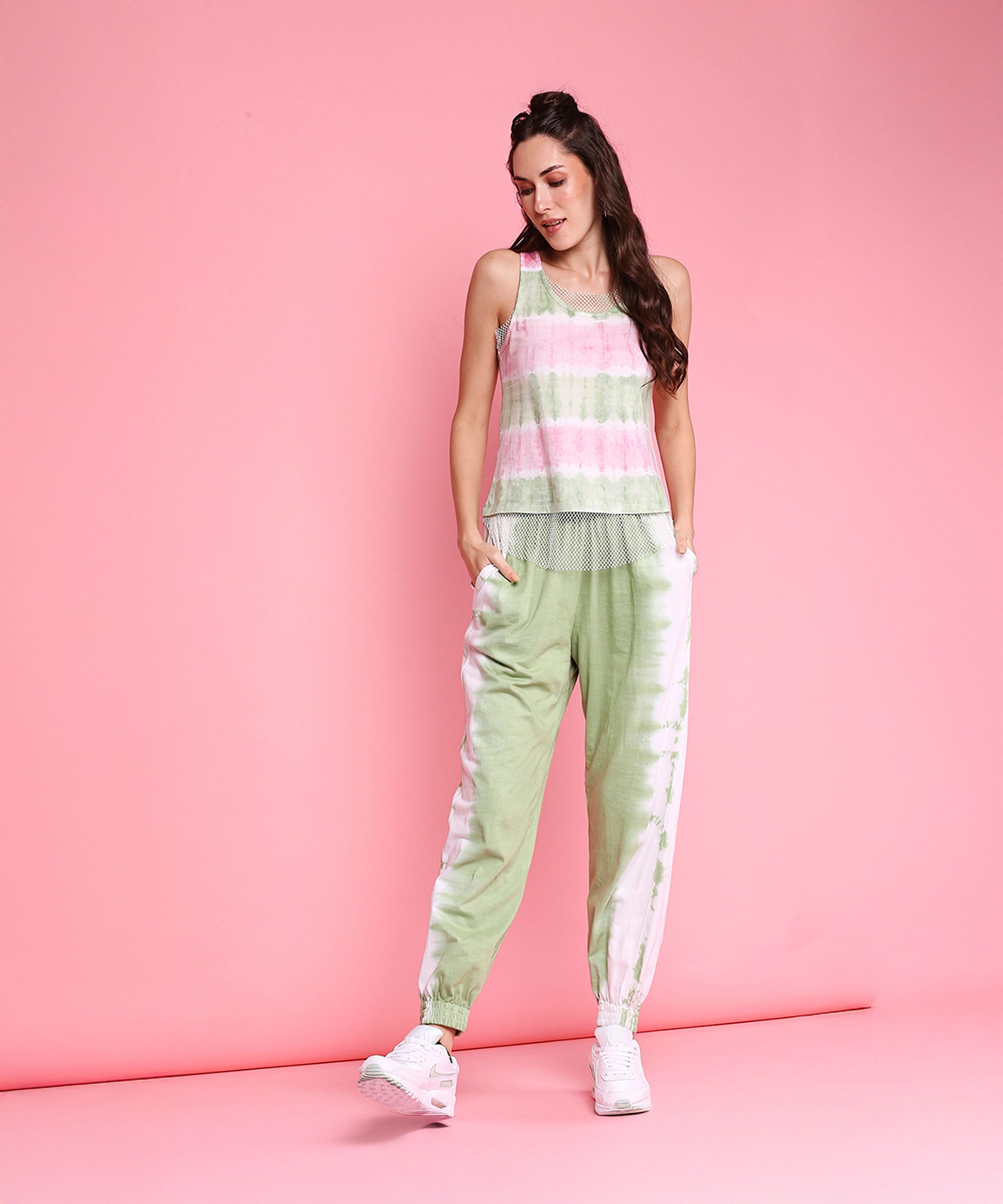 A woman in the Comfort Fit Joggers + Netted Tank Top - AW21 stands against a pink background, looking down and smiling.