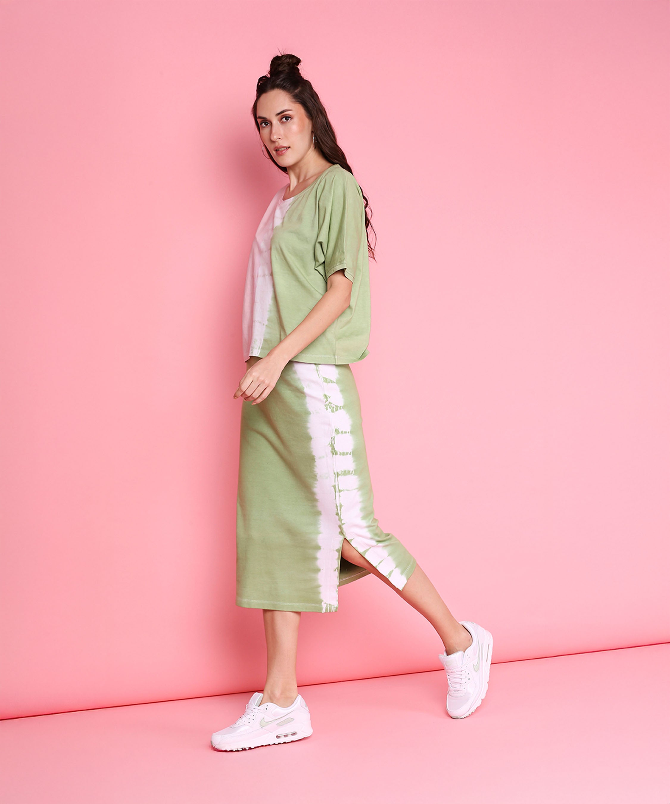 Woman wearing the Comfort Fit Tee + Fitted Tie Dye Skirt - AW21 in pastel pink and mint green, paired with white sneakers, poses against a pink background.