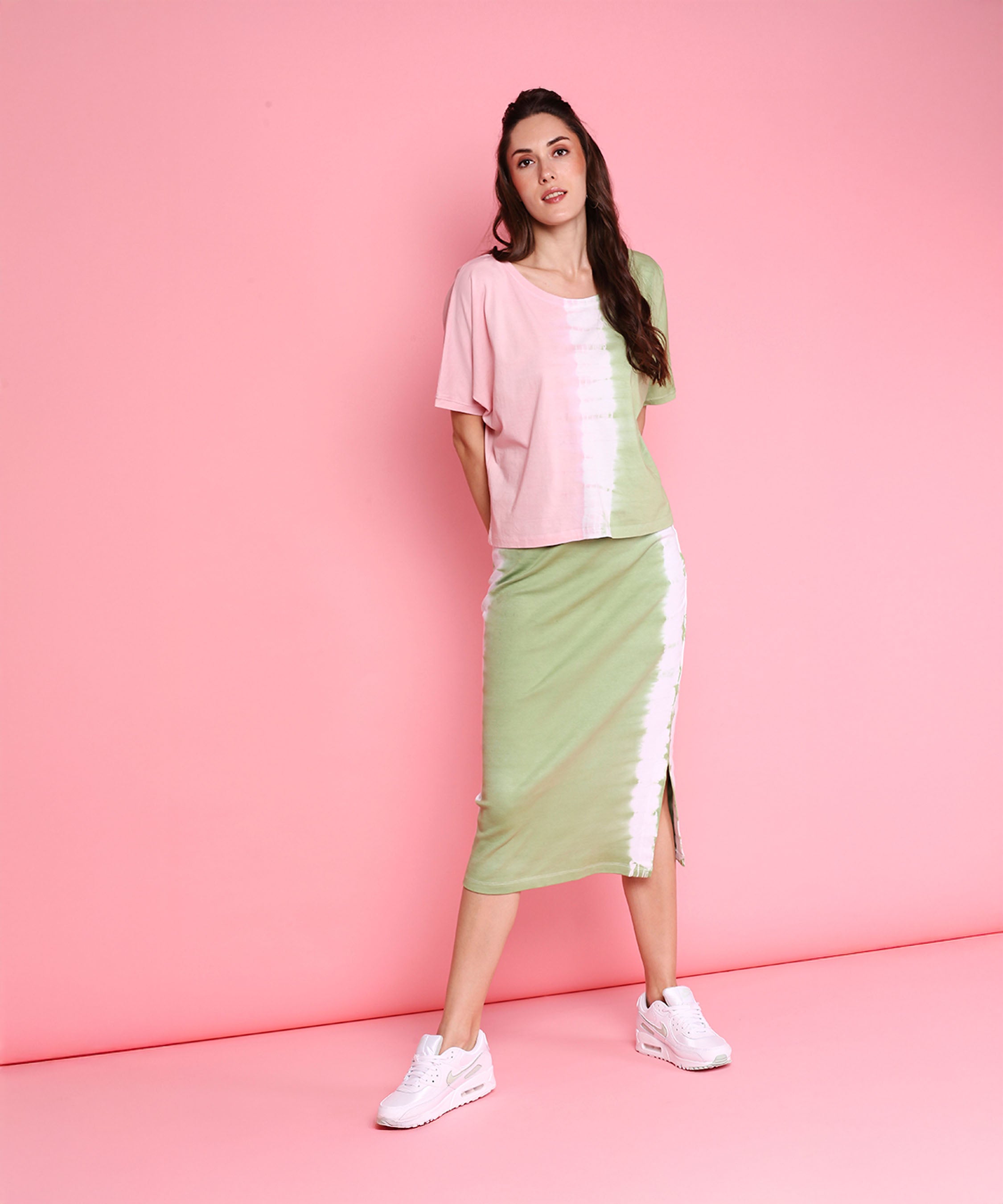 Woman wears the Comfort Fit Tee and Fitted Tie Dye Skirt - AW21 with white sneakers, posing against a pink background for a fresh athleisure vibe.