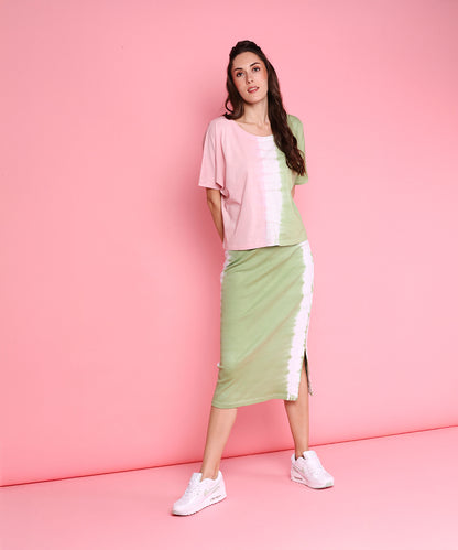Woman wears the Comfort Fit Tee and Fitted Tie Dye Skirt - AW21 with white sneakers, posing against a pink background for a fresh athleisure vibe.