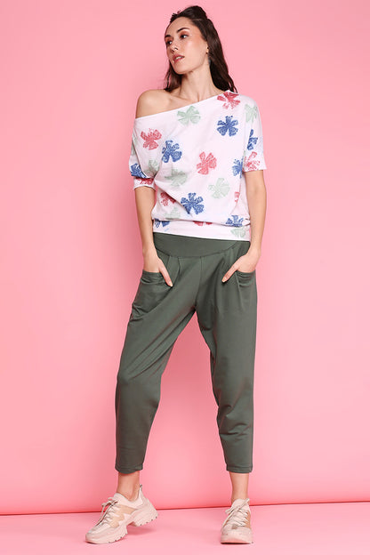 A woman in Pleated Yoga Pants - AW21, a floral off-shoulder top, and sneakers poses against a pink background, embodying an effortless Autumn/Winter 21 style.