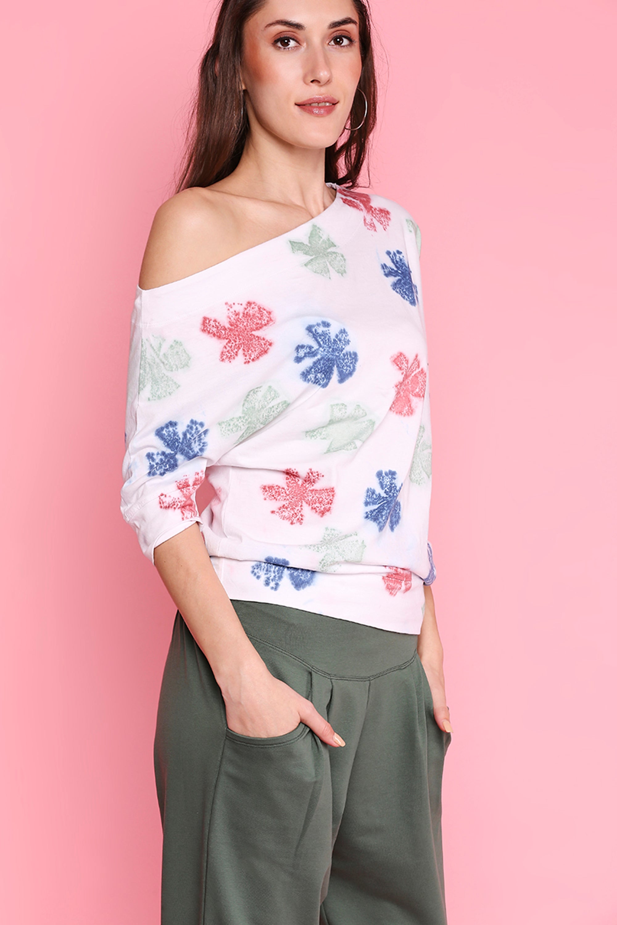 Woman in a floral off-shoulder top and Pleated Yoga Pants - AW21, posing against a pink background. Ideal for an Autumn Winter 21 look.