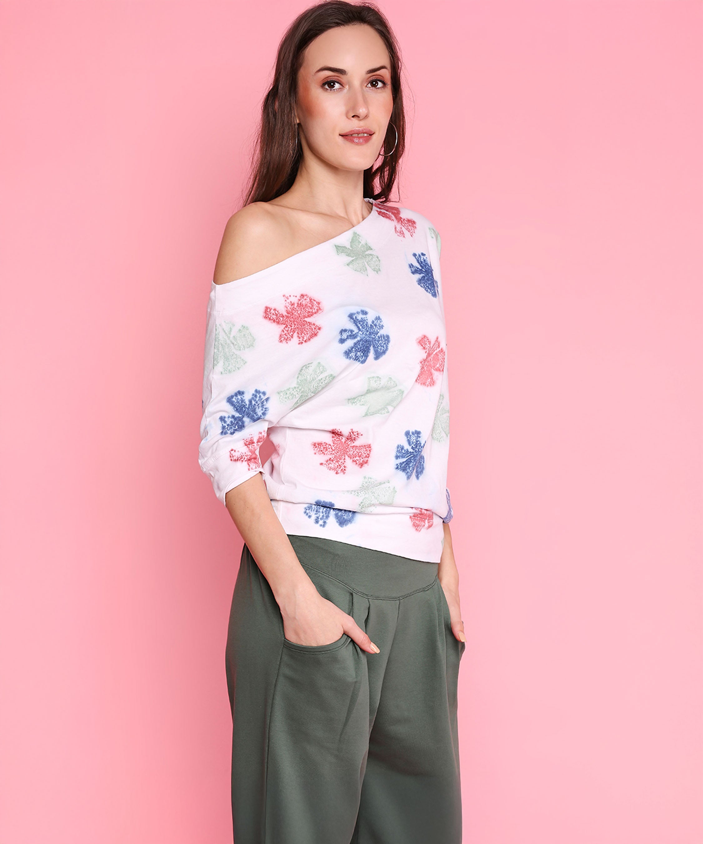 A woman models the One Side Off Shoulder + Pleated Yoga Pants - AW21, standing against a pink background with hands casually in her pockets.