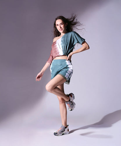 Woman models the Oversized Comfort Tee + Shorts - AW21 set, paired with sneakers, against a softly lit plain background.